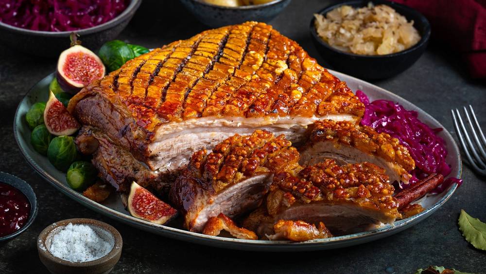 Ribbe med sprø svor, servert med rosenkål, poteter, surkål og julekrydder på et fat.