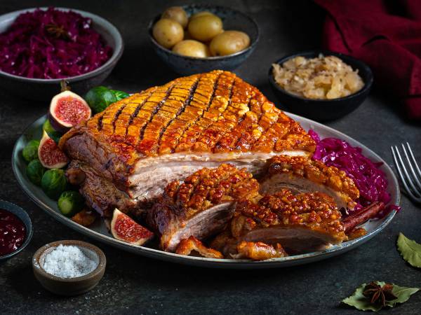 Ribbe med sprø svor, servert med rosenkål, poteter, surkål og julekrydder på et fat.