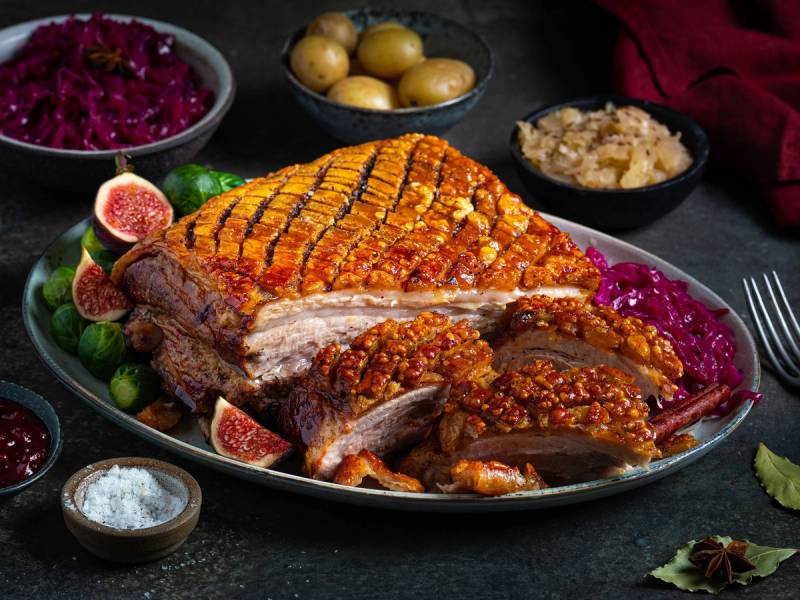 Ribbe med sprø svor, servert med rosenkål, poteter, surkål og julekrydder på et fat.