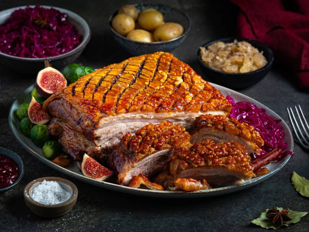 Ribbe med sprø svor, servert med rosenkål, poteter, surkål og julekrydder på et fat.