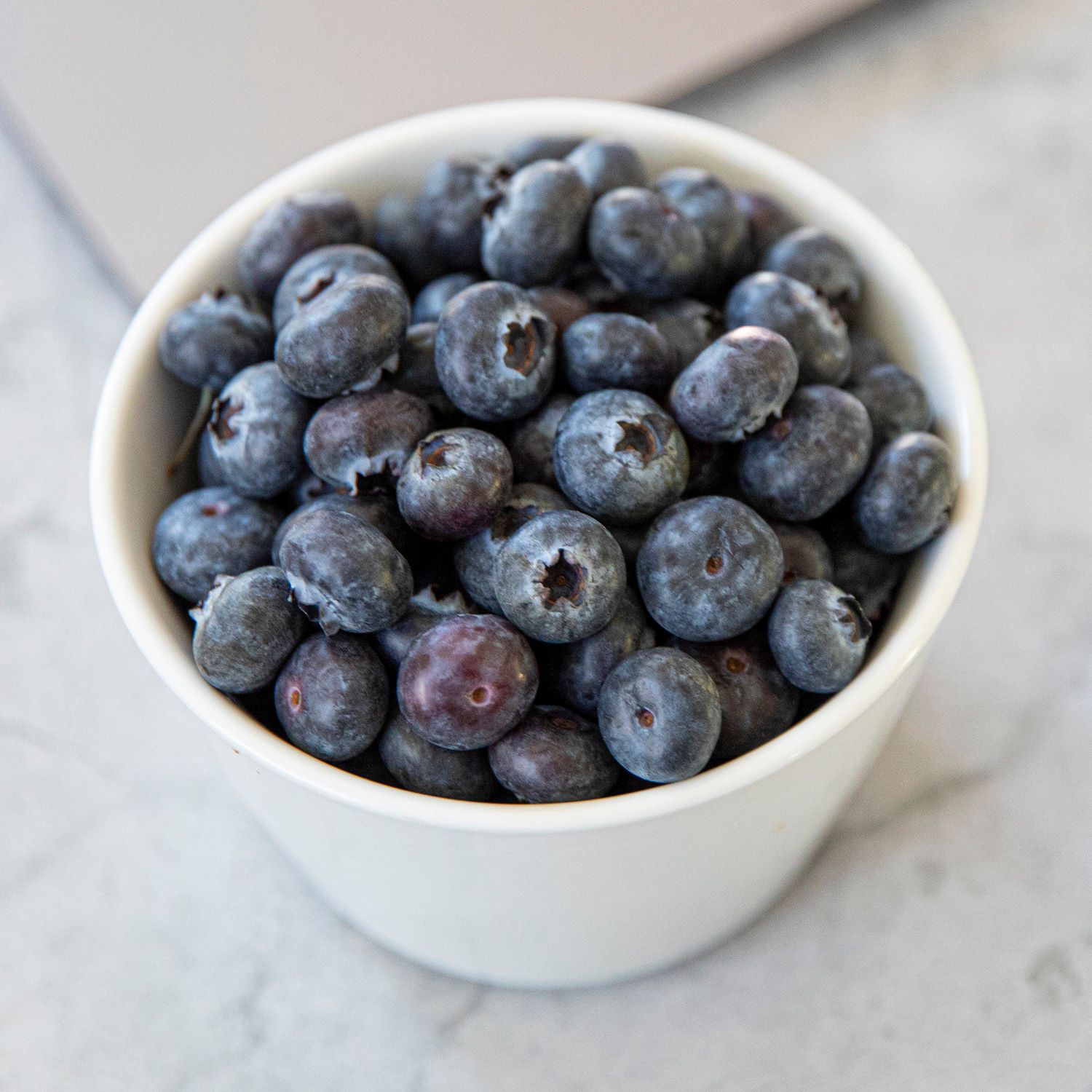 En hvit kopp fylt med blåbær på en lys overflate