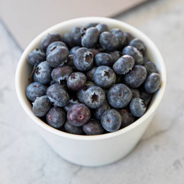 En hvit kopp fylt med blåbær på en lys overflate
