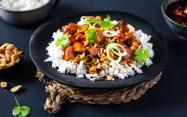 Kylling Gong Bao servert med ris og garnityr av nøtter og grønnsaker på en svart tallerken