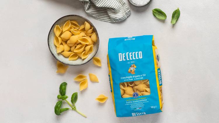 Pakkede DeCecco-pasta med noen løv og et kjøkkenhåndkle i bakgrunnen.