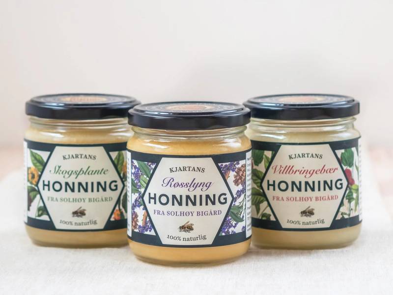 Tre glass med honning fra ulike norske produsenter, plassert på en hvit bakgrunn.