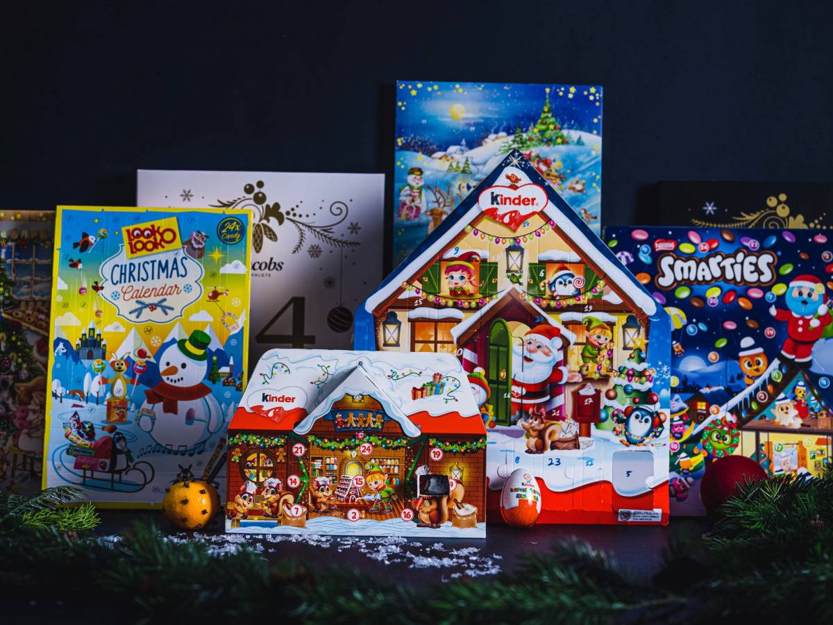 Ulike julekalendere med vinter- og julestemning, plassert på en mørk bakgrunn med noen grønne grener foran.