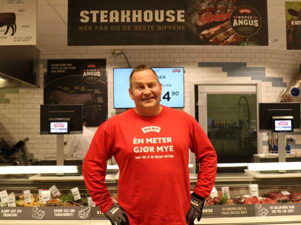 Person i rød genser foran kasseområde i en butikk, med menyer og skjermer i bakgrunnen.