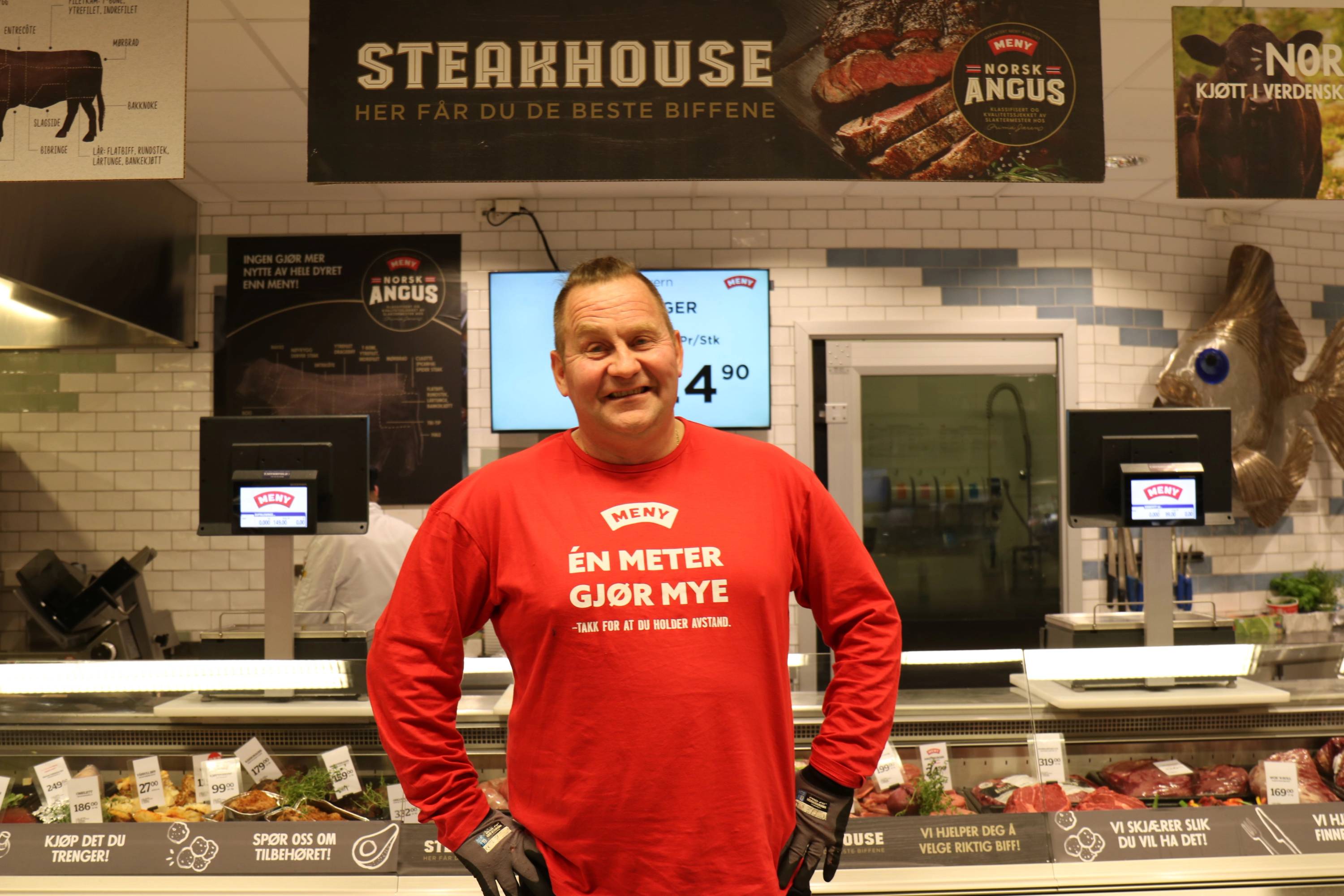 Person i rød genser foran kasseområde i en butikk, med menyer og skjermer i bakgrunnen.