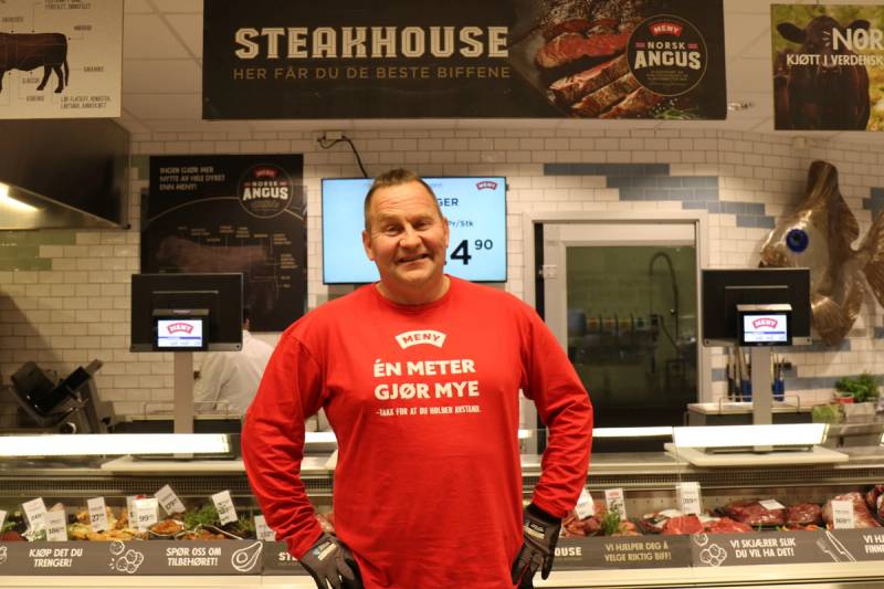 Person i rød genser foran kasseområde i en butikk, med menyer og skjermer i bakgrunnen.