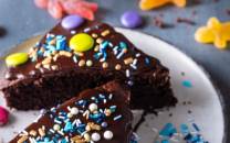 En langpanne med sjokoladekake som har et stykke tatt ut, pyntet med fargerike sukkerper og strøssel.