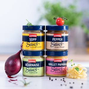 Fire små glass med Eldorado-sauser i ulike smaker, plassert på en hvit overflate med en rød løk og noen krydder rundt.