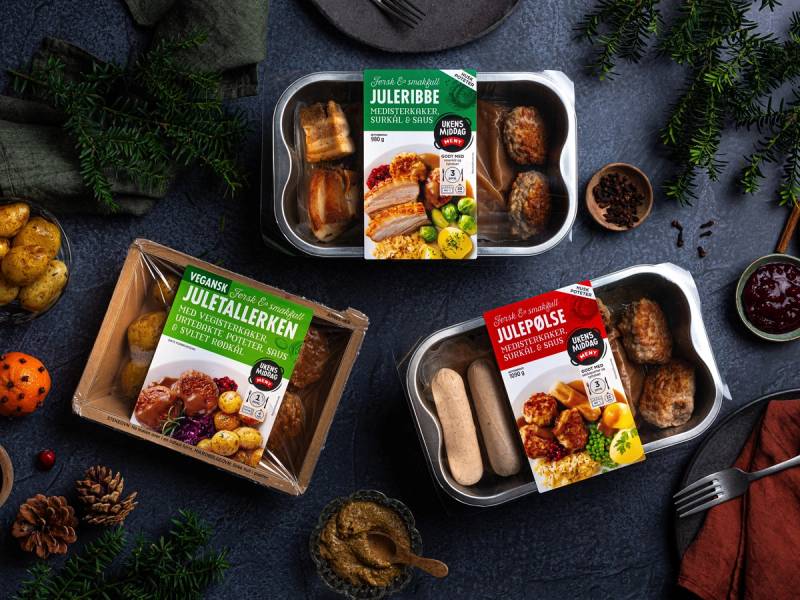 Juletallerken med julepølse, juleribbe og annet julemat, omgitt av granbar og juledekorasjoner.