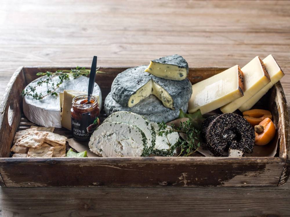 Et ostefat med ulike typer ost, inkludert blåmuggost, hvit ost og en mørk ost, plassert i en trekasse.