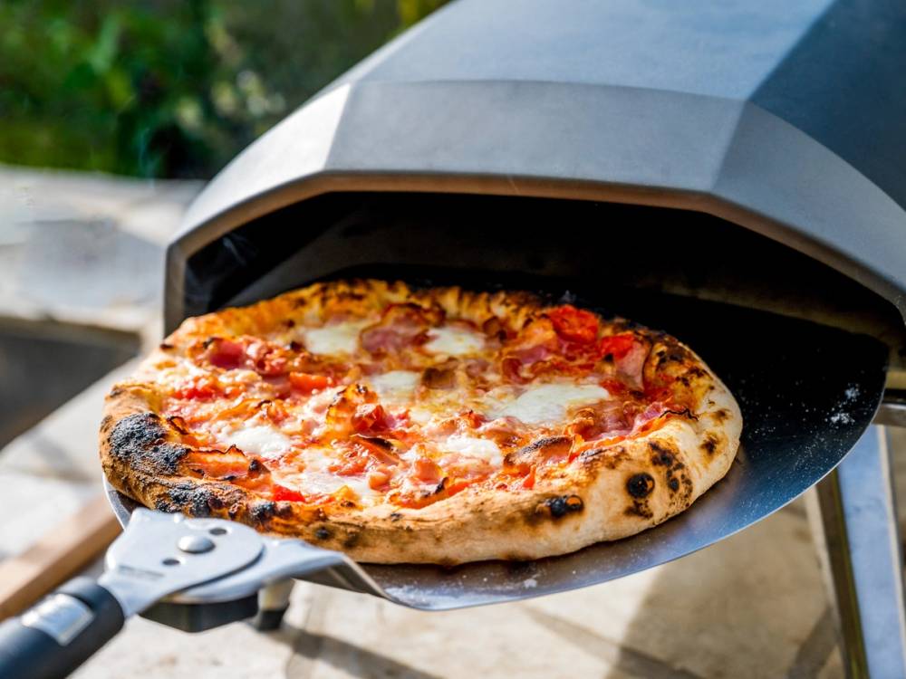 En pizza med ost, tomatsaus og skinke som blir bakt i en ovn utendørs.