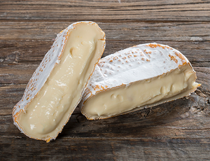 To stykker ost med hvit skorpe på en treoverflate, hvorav den ene er delt i to.