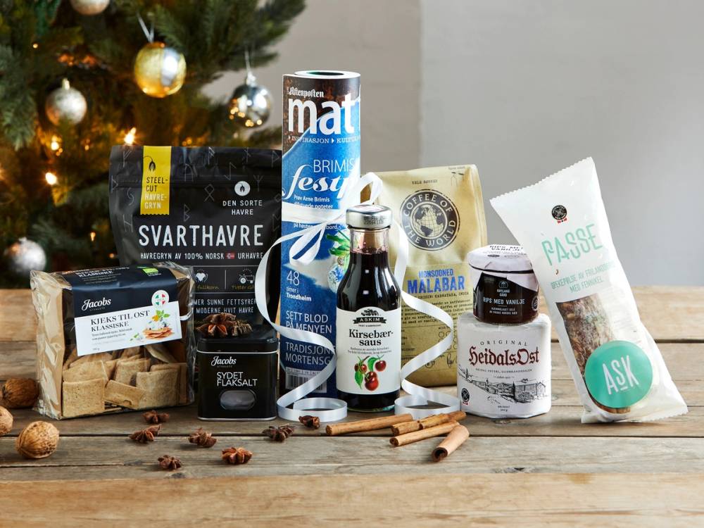 Et utvalg av matvarer og julepynt på et bord, inkludert kaffe, sjokolade, krydder og en liten julegran med pynt.