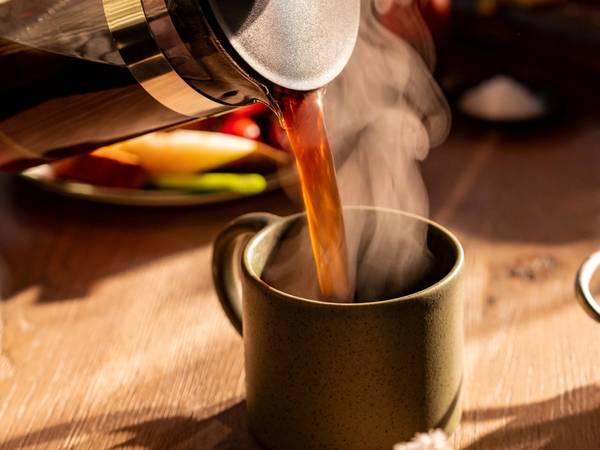 Kaffe helles fra en presskanne opp i en svart kopp med damp som stiger opp.