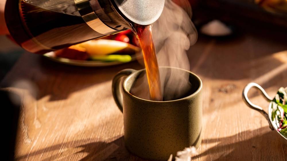 Kaffe helles fra en presskanne opp i en svart kopp med damp som stiger opp.