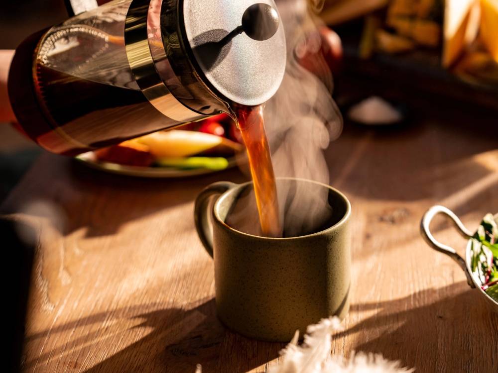 Kaffe helles fra en presskanne opp i en svart kopp med damp som stiger opp.