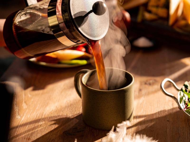 Kaffe helles fra en presskanne opp i en svart kopp med damp som stiger opp.