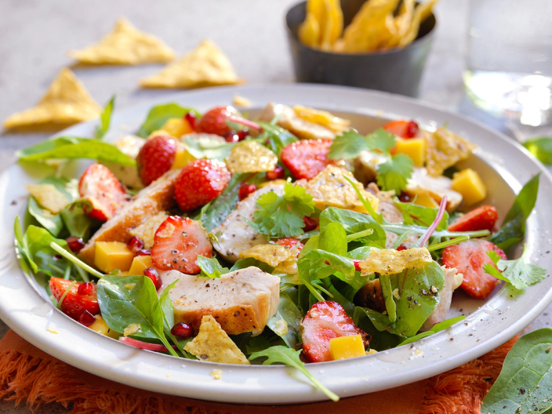 En frisk salat med jordbær, mango, kylling og tortilla chips på en hvit tallerken.