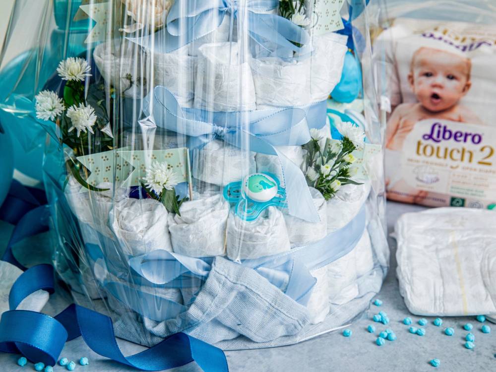 En bleiekake dekorert med blomster og små leker, omgitt av bleier og babyprodukter.