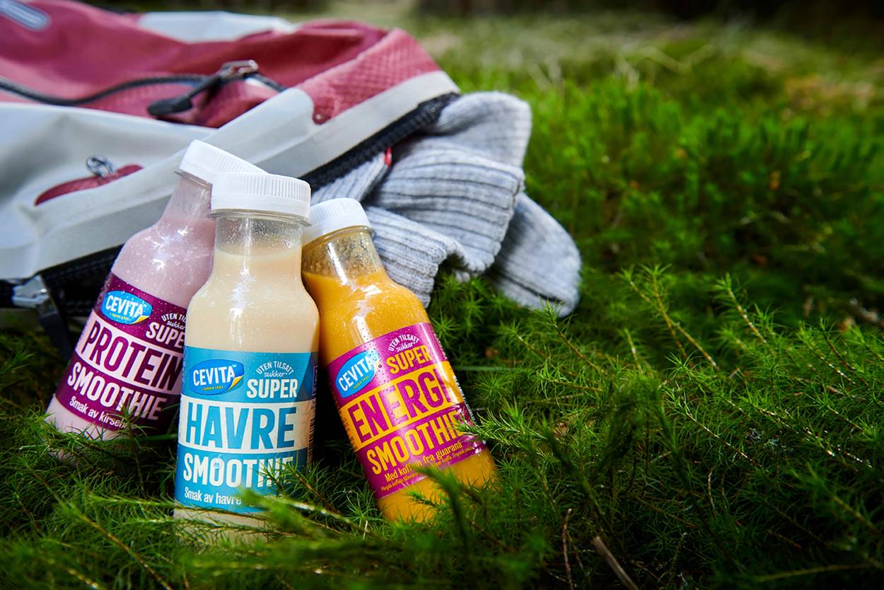 To Cevita-super smoothies, en med havre og en energifokusert, ligger på gress med klær i bakgrunnen.