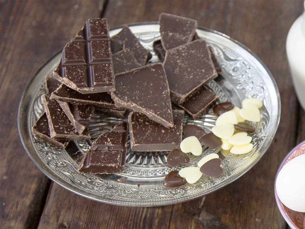 Ulike typer sjokolade i biter på et glassfat med noen hvite sjokoladeknapper ved siden av