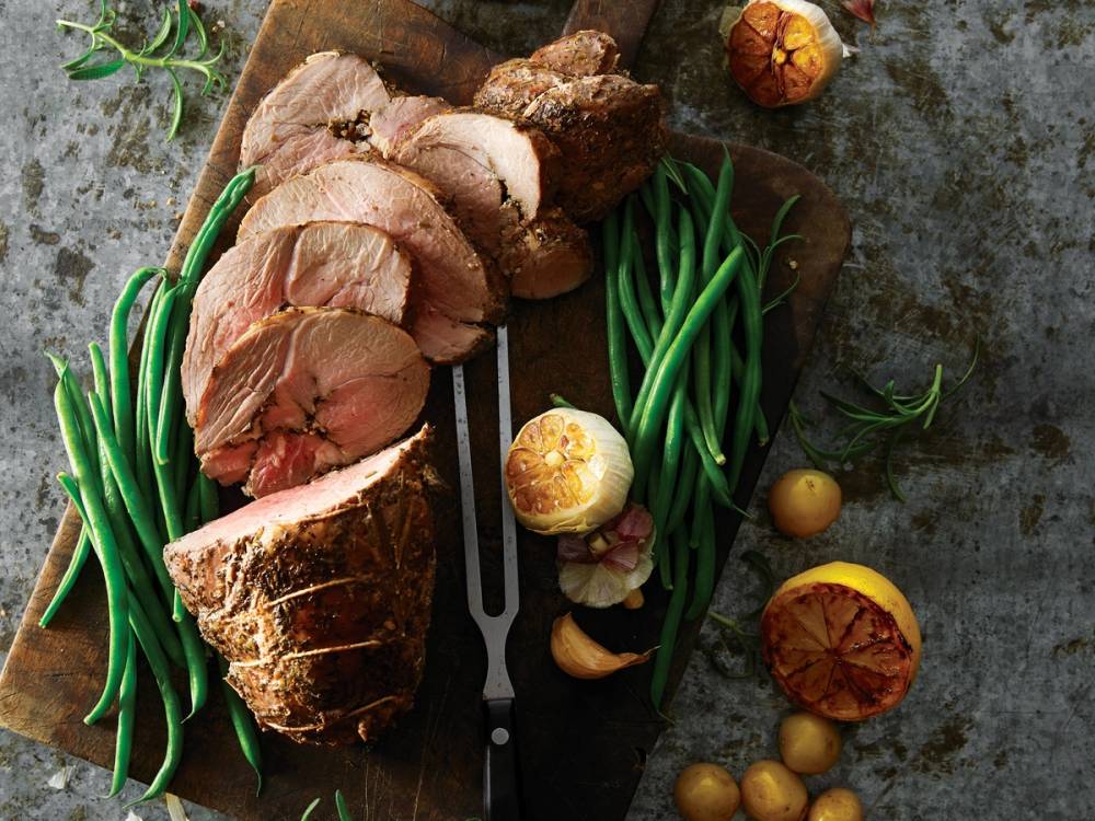 Skarpt skåret lammestek med grønne bønner og små poteter på et skjærebrett.