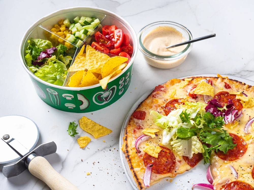 Salatbar med grønnsaker og sitrusbiter ved siden av pizza på et bord.