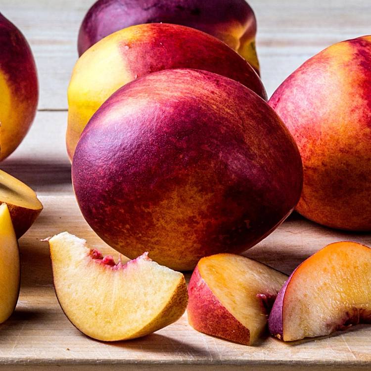 Ferske nektariner og noen skiver av dem ligger på et lyst trebord.