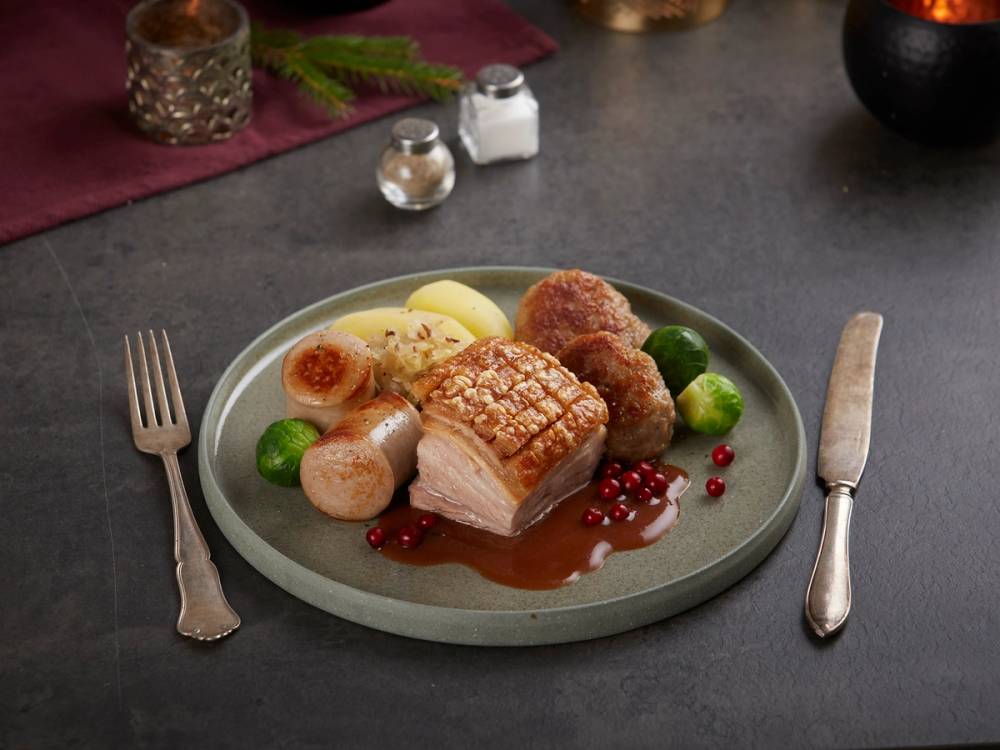 Ribbe med julekål, poteter og tyttebær på en tallerken, med bestikk på hver side.