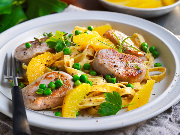 Pasta med svinefilet, appelsinbåter og grønne erter på en hvit tallerken