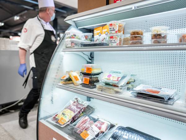 En person i butikk som ser på matvarer i en kjøledisk, med fokus på mat for å redusere matsvinn.