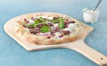 Eltefri pizza med reinsdyrskav, granateple og spinat på et skjærebrett med en liten skål med saus ved siden av.