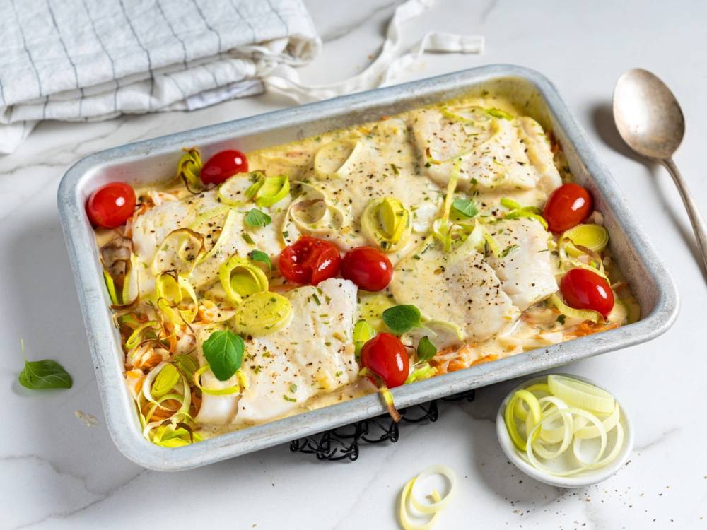 Torsk i ovn med cherrytomater og grønne løk, servert i en ildfast form.