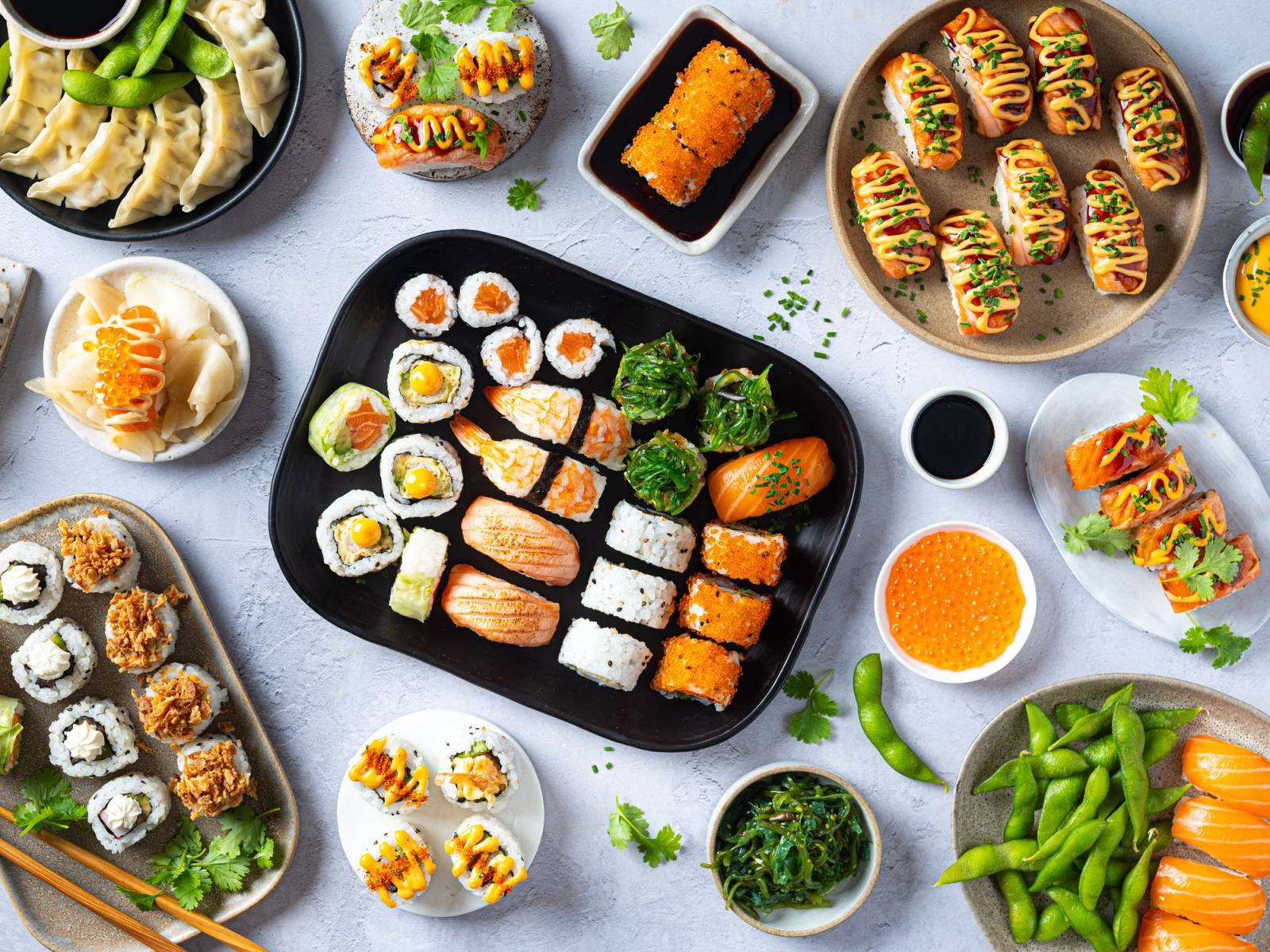 Et utvalg av sushi på ulike tallerkener, inkludert nigiri, maki og ruller, med grønnsaker og saus rundt.
