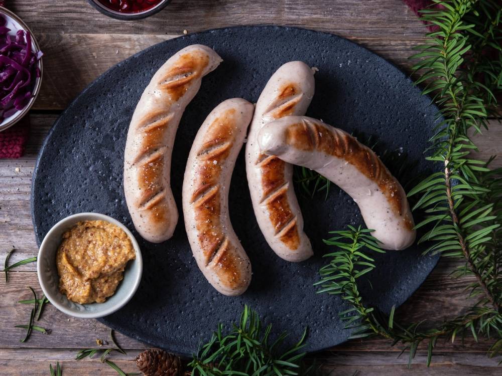 Medisterpølser på en svart tallerken med sennep og grønn dekorasjon rundt, klar til servering.