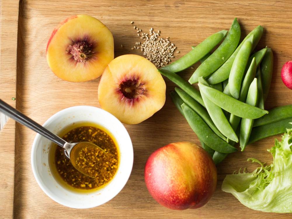 Fersken, nektarin og sukker på et skjærebrett med en skål med olje eller saus, og en liten salat, på et treverk.