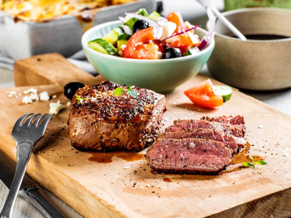 Grillet biff skåret opp på skjærebrett med en frisk salat i bakgrunnen.
