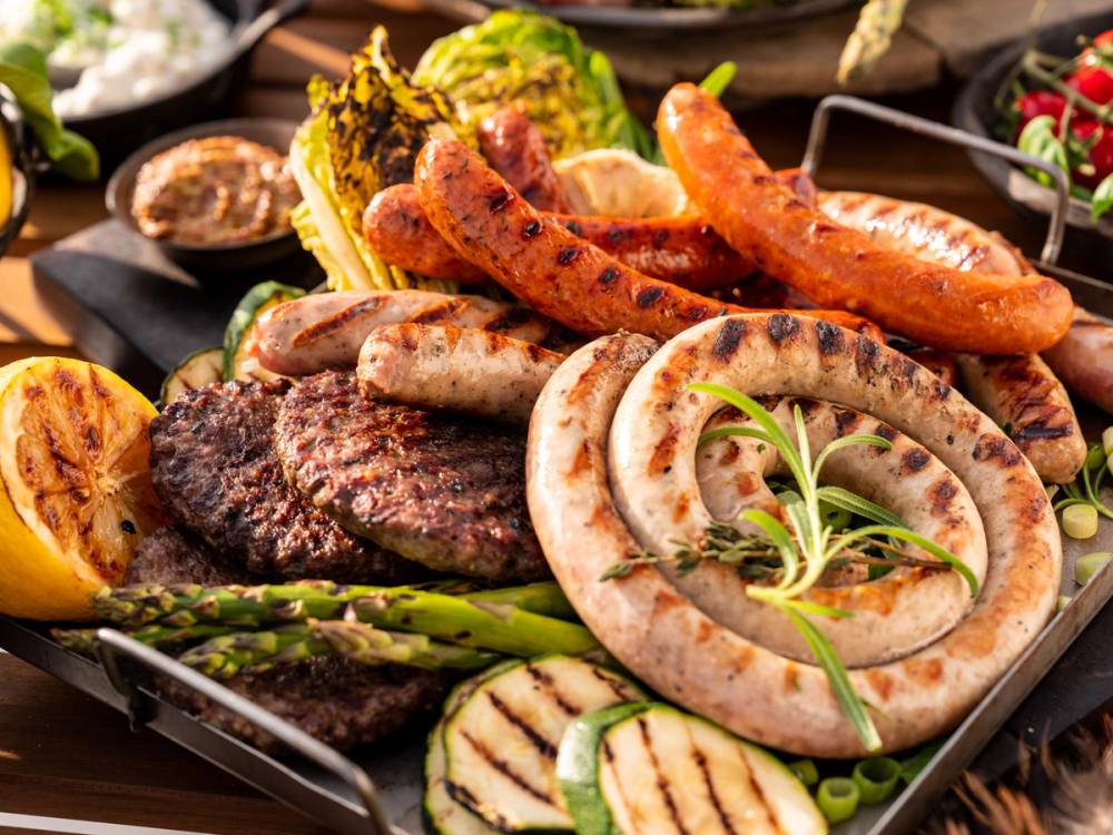 Grillmat med ulike kjøttstykker og grønnsaker på en grillplate.