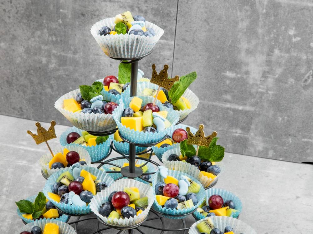 En treetasjes kakefat med små cupcakes pyntet med frukt og grønne blader, dekorert til babyshower.