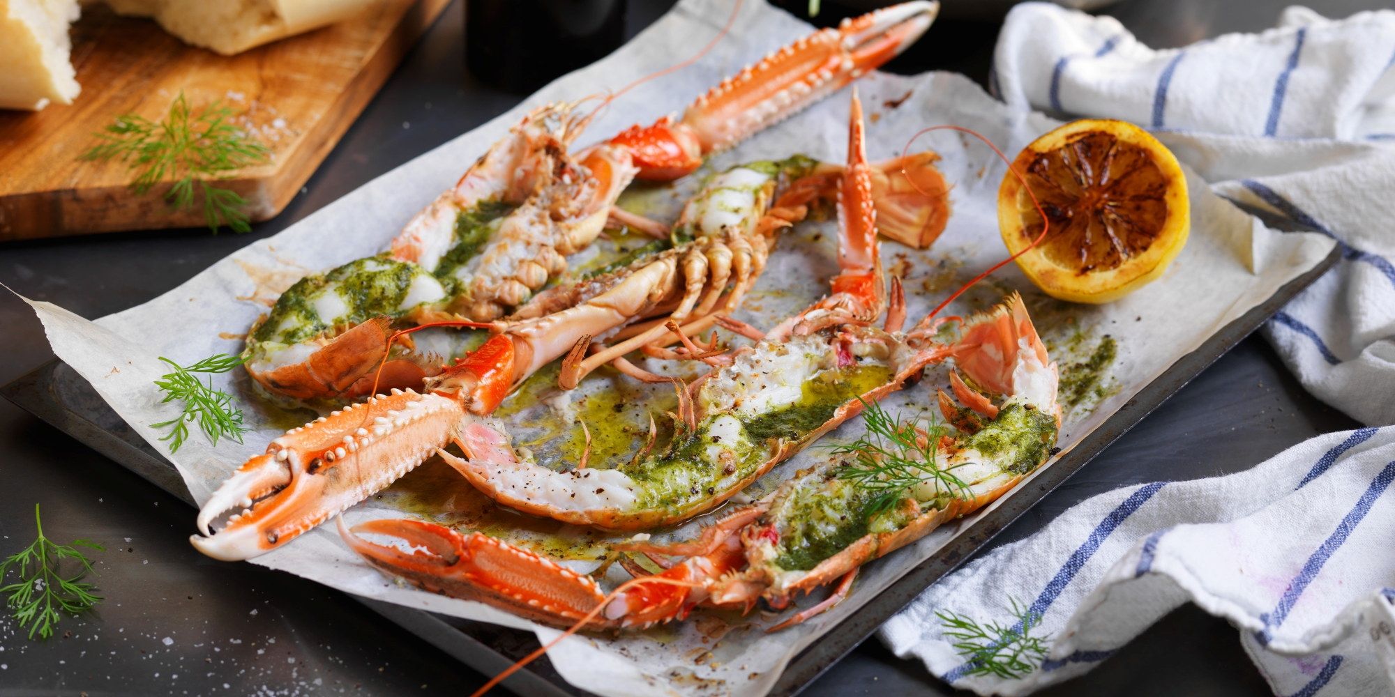 Gratinerte sjøkreps med ramsløksmør servert på et fat med sitronbåter og urter, klar til å spises.