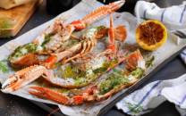 Gratinerte sjøkreps med ramsløksmør servert på et fat med sitronbåter og urter, klar til å spises.