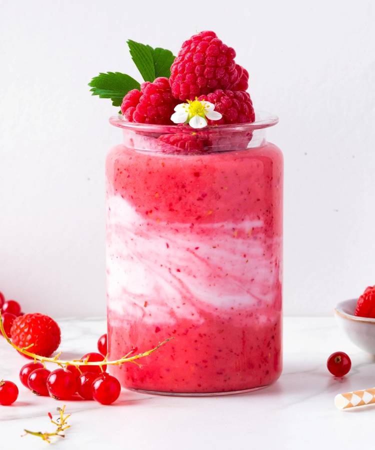 Bringebær- og ripssmoothie i et glass med friske bær og mynte på toppen