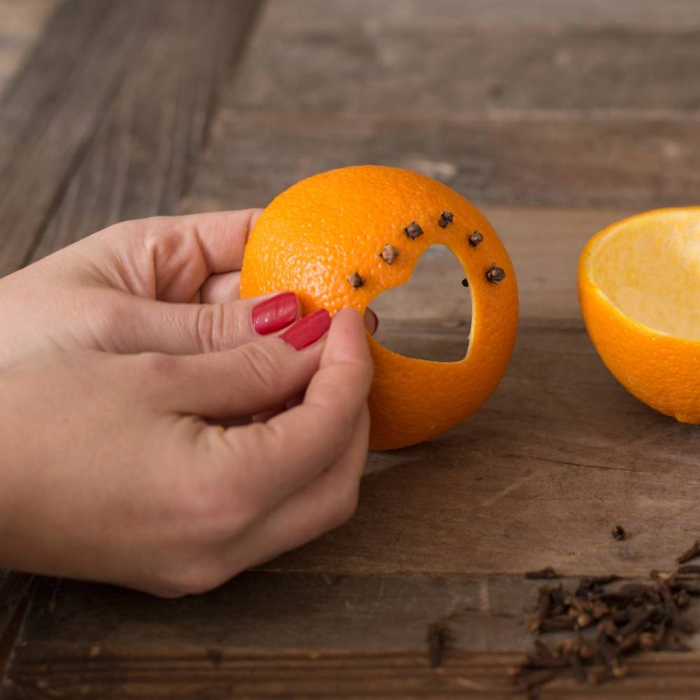 En person holder en klementin med hull i skallet, som er laget til en liten krok, på et trebord med en halvert klementin ved siden av.