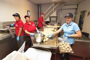 Fire personer jobber sammen i et kjøkken, hvor de lager eller pakker matballer, med fokus på arbeidsoppgaven og utstyret rundt dem.