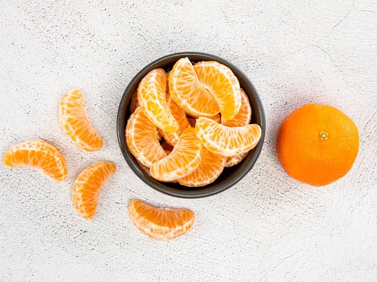 En svart skål med oppdelte mandariner og en hel mandarin ved siden av på en lys bakgrunn.