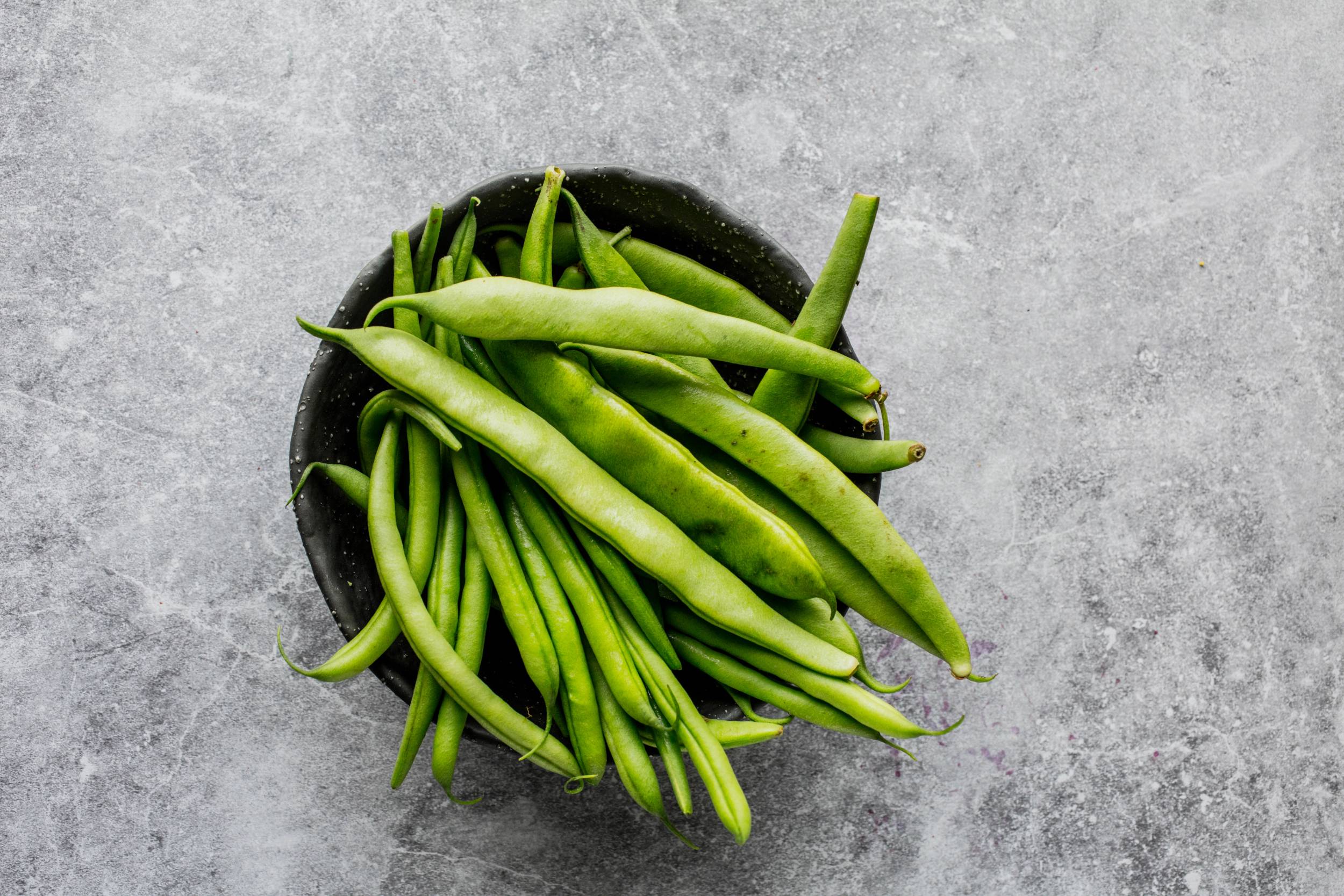En svart bolle fylt med friske grønne bønner på en grå overflate