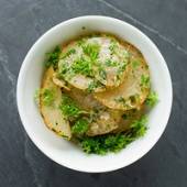 Poteter som er kokt og ser ut til å være krydret med urter, ser ut til å være i en hvit bolle på en mørk overflate.